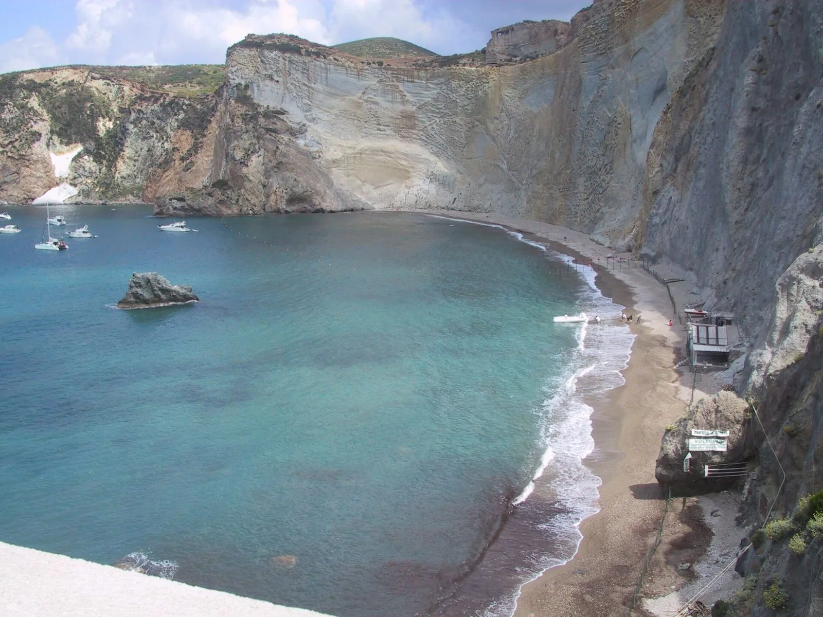 La baia di Chiaia di Luna a Ponza vista dall'alto, con la spiaggia stretta ai piedi di un'alta falesia chiara, il mare turchese e alcune barche ancorate nella baia